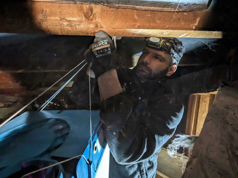 Technicien en combinaison noire équipé d'une lampe frontale et de gants de travail **Force** (modèle FR856 C&G), travaillant dans un espace de combles exigu
